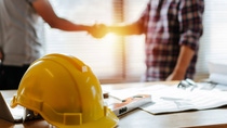 Gros plan d’un casque sur une table de chantier avec deux personnes se serrant la main en arrière-plan. Gros plan d’un casque sur une table de chantier avec deux personnes se serrant la main en arrière-plan.