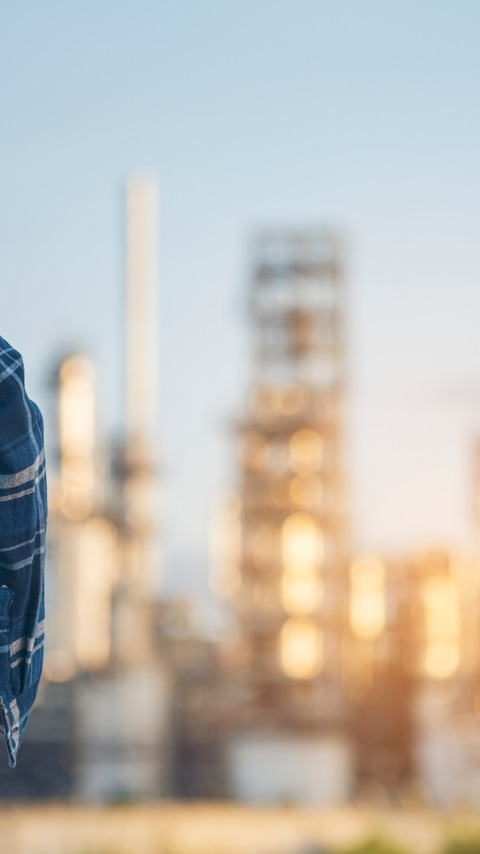 Image of an industrial site with a person holding a hard hat in the foreground