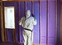 Installer spraying WALLTITE purple spray foam insulation into a wall cavity.
